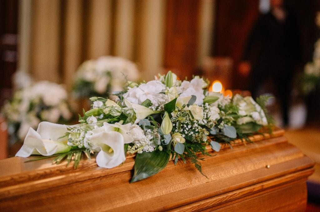 A coffin decorated with many flowers and candles in a beautiful church, ceremony