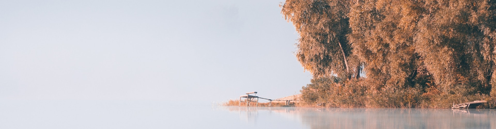 Panorama of calm autumn lake with fog over water and reflections of trees. Wooden jetty for fishing on the lake coast.